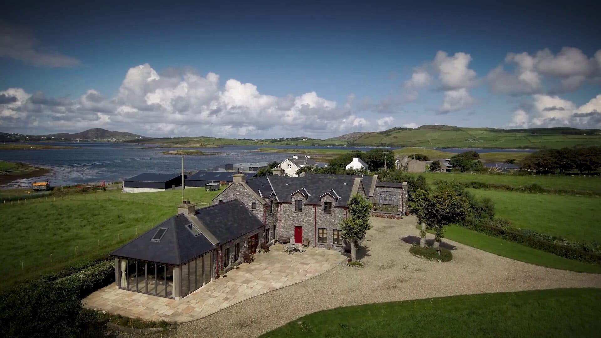 Aerial view of a stone house with a glazed sun room beside a sea inlet in Donegal